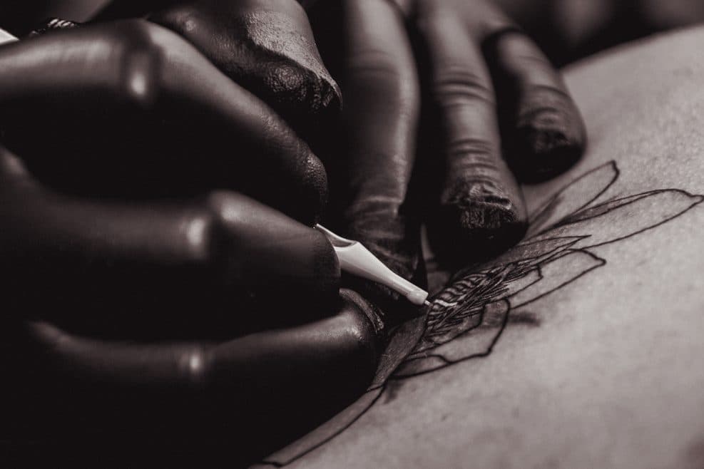 Mains gantées traçant un motif à l'encre sur la peau